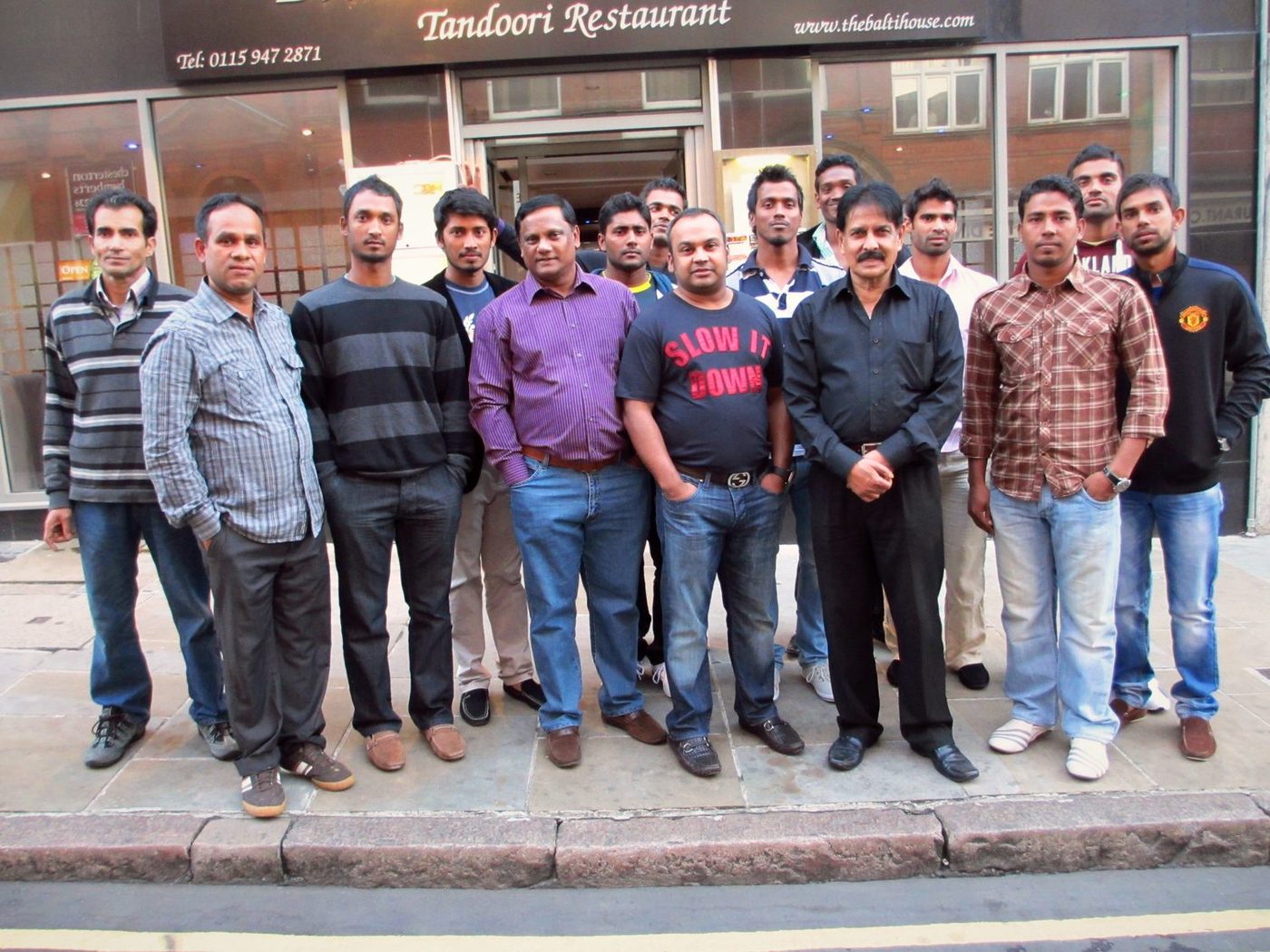 A large group photographed outside The Balti House beneath the Tandoori Restaurant sign
