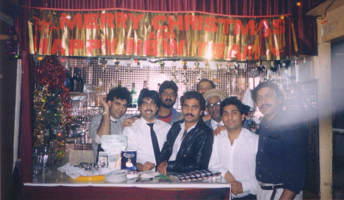 Nine staff crowded behind the Balti House bar under a Merry Christmas banner in the 1980s