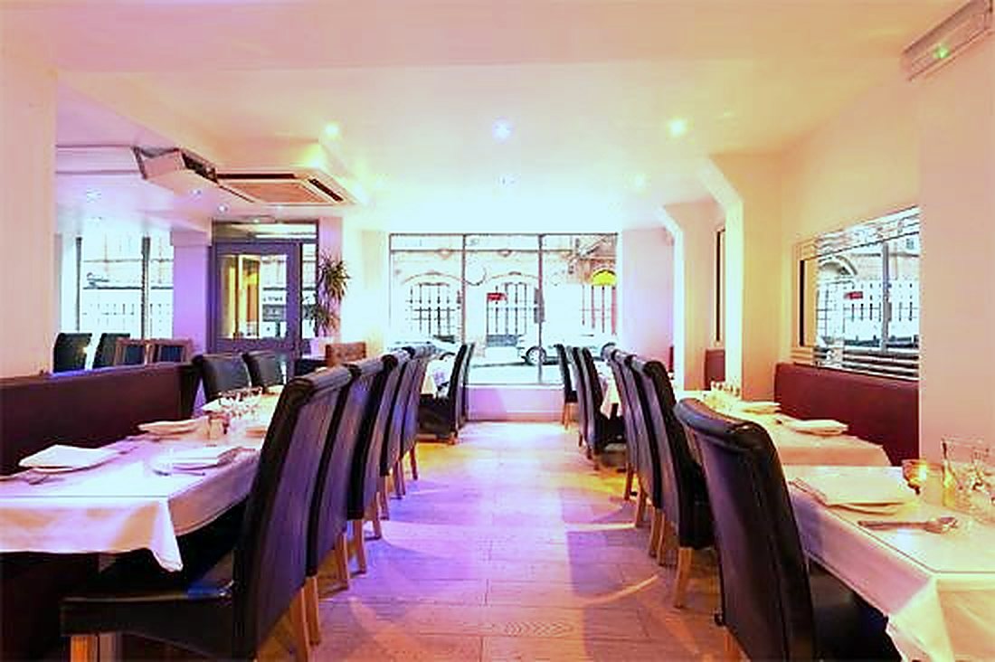 The Balti House dining room laid for service — white linen, leather chairs and a full glass frontage onto Heathcoat Street