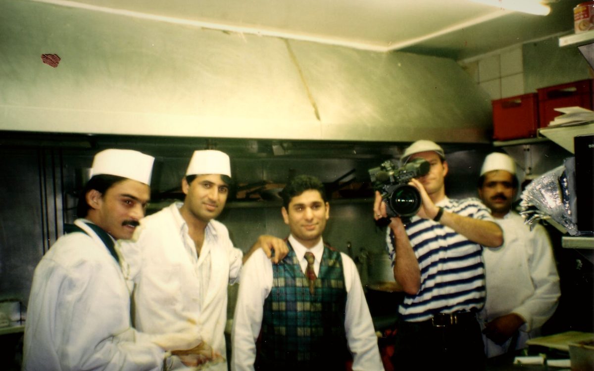Balti House chefs in whites beside a cameraman filming in the kitchen, 1995