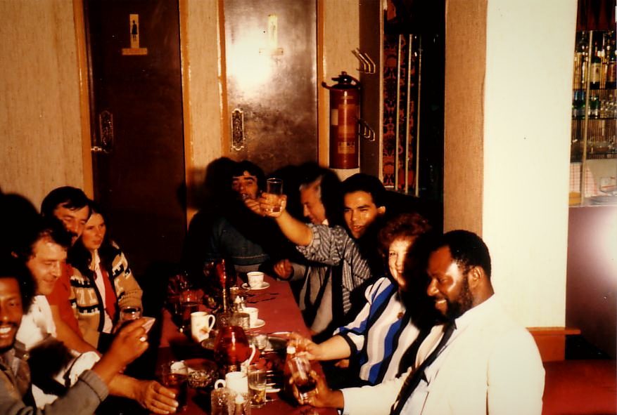 A mixed group of diners raising glasses around a long red table at The Balti House in the 1970s